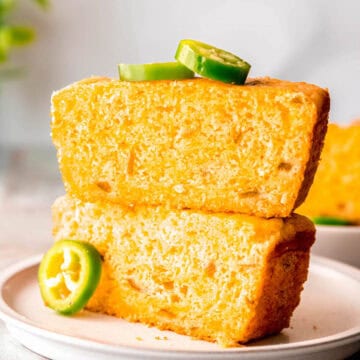 two slices of jalapeno cheddar jiffy cornbread stacked atop one another on a white plat with fresh slices of jalapeno as garnish.