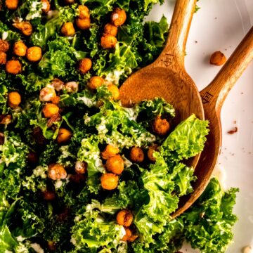 square overhead closeup of chickpea tahini fall kale salad with two wooden serving spoons.