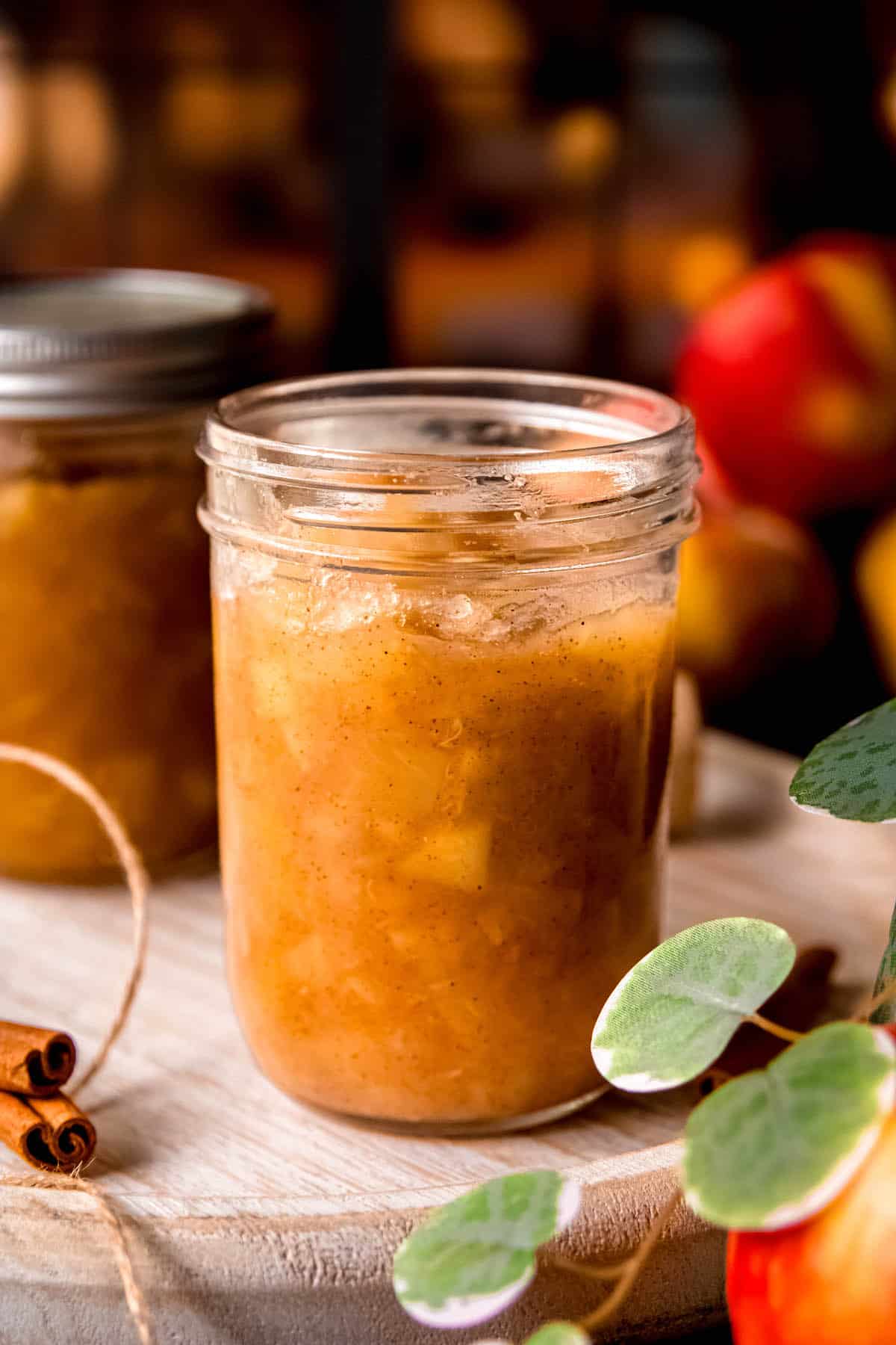 an opened jar of homemade apple pie filling after canning sitting on a table with fresh multicolored red and yellow apples.