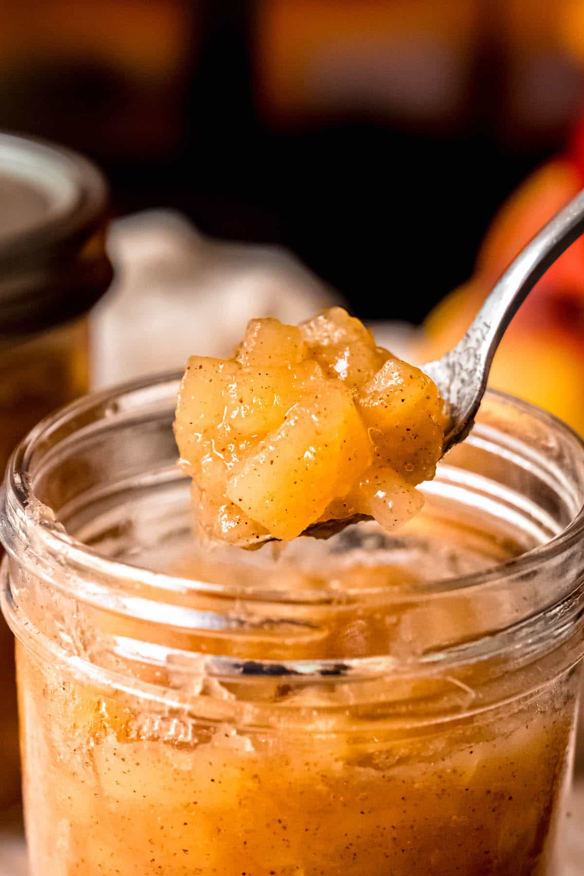 closeup of a silver spoon with a bite of chunky apple sauce hovering above the mason jar it was canned in.