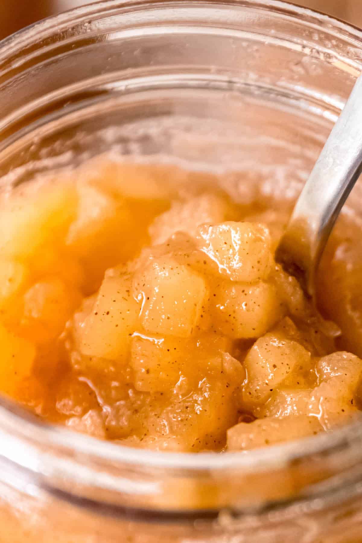 hyper closeup shot of chunky cinnamon apple jam in a glass jar with a silver spoon sticking out.