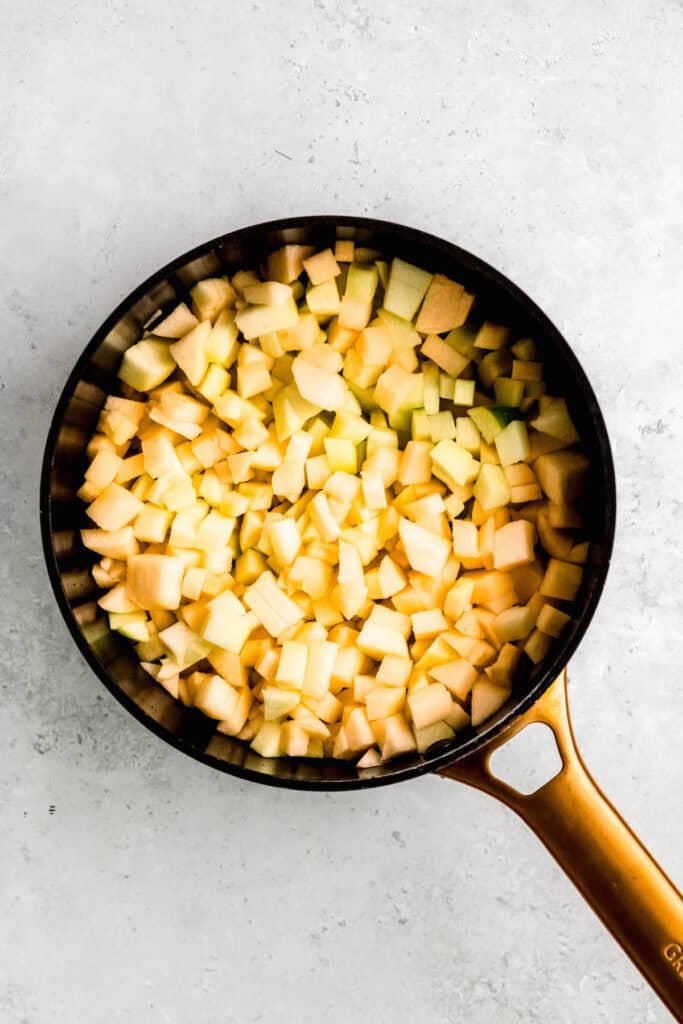 washed, peeled, and diced apples added to a black saucepan with a gold-brass handle.