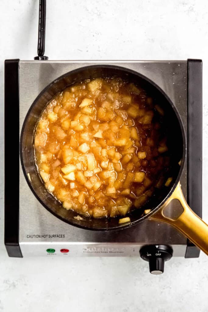 saucepan filled with chunks of cinnamon apple preserves after cooking until the apples are soft and the liquid is dark and thick after concentrating.