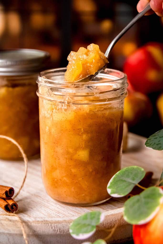 spoon filling a sterilized mason jar with homemade applesauce.