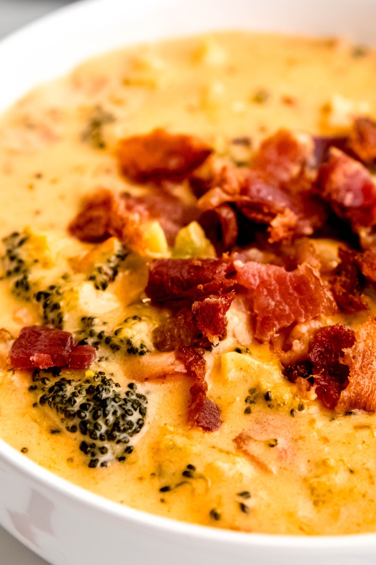 closeup shot on the middle slice of a round white bowl filled with bacon broccoli cheddar cheese soup topped with extra bacon bits.