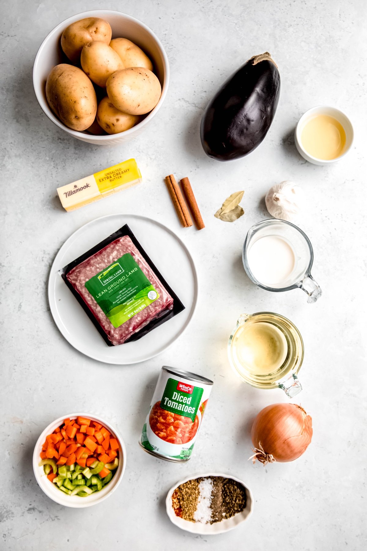 ingredients needed to make Greek gluten-free shepherds pie with ground lamb and eggplant measured out on a white table.
