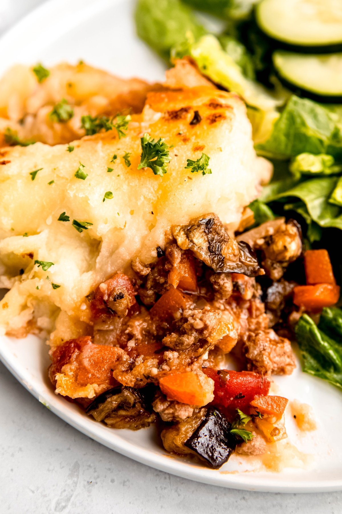 closeup shot of the ground lamb eggplant moussaka filling of the gluten free cottage pie with the potato layer to the top side of the frame revealing the crispy caught edges of potatoes atop the creamy mashies base.