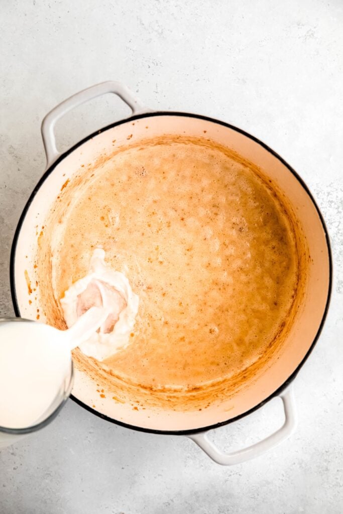action shot of milk and cream being added to the pot with the light golden roux.