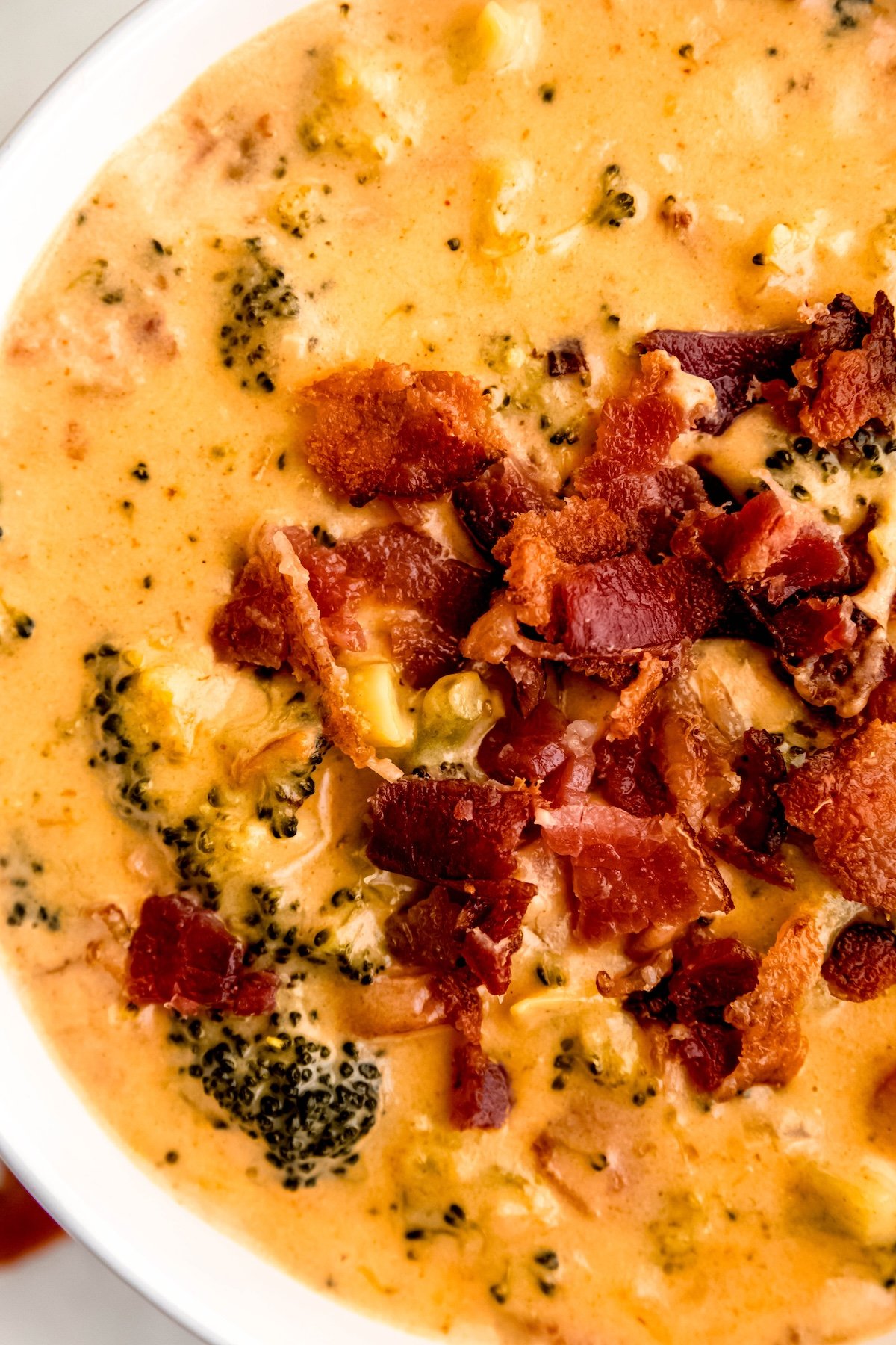 closeup overhead shot of a serving of broccoli cheese soup topped with crispy bacon bits; you can see the texture of the soup from the broccoli florets and carrot rounds.