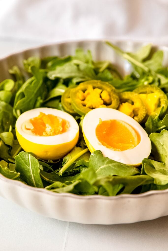 halved jalapeno pickled egg on a bed of arugula with some of the pickled jalapeños.