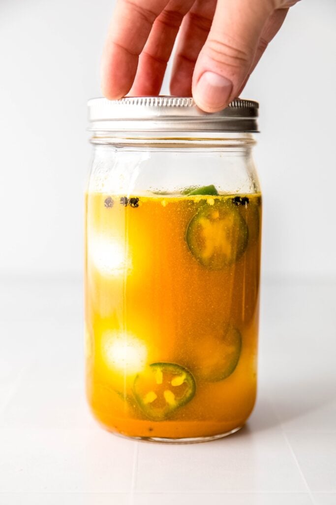 hand screwing on the lid of the mason jar after adding the eggs to pickle.