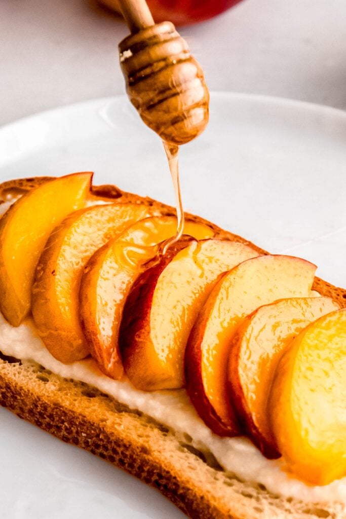 closeup shot of honey dipper drizzling honey onto peach toast.