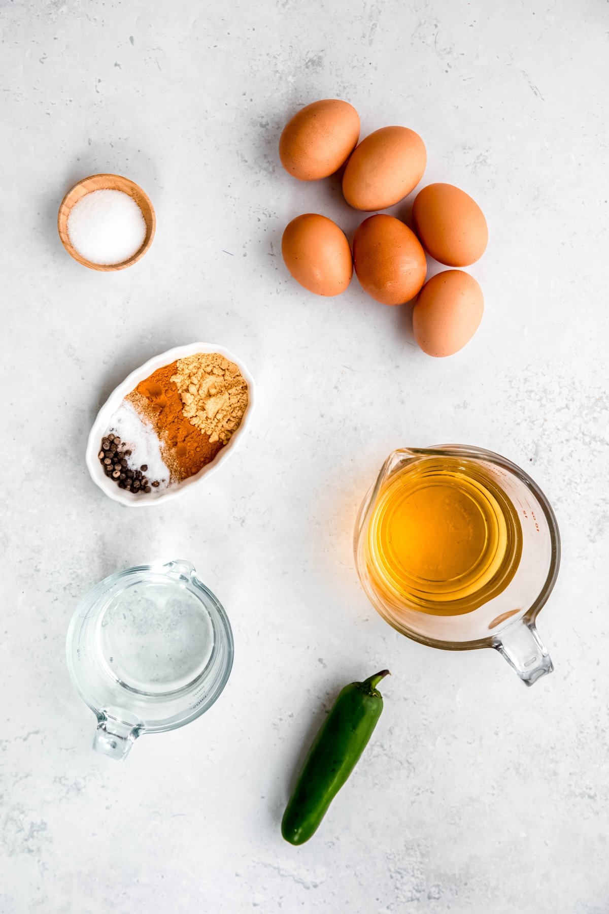 ingredients for making pickled eggs with jalapeños and turmeric measured out on a white table.