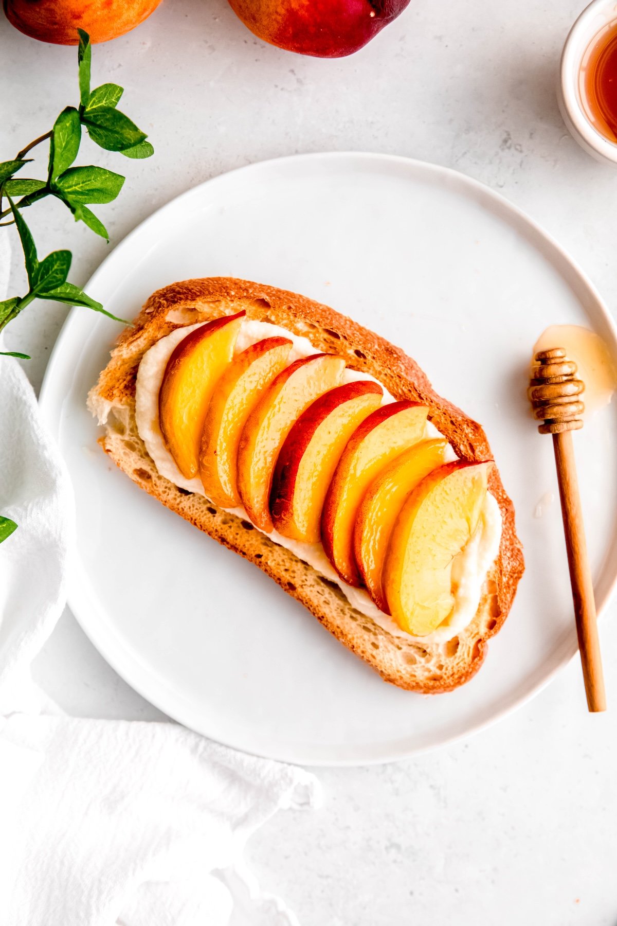 overhead shot of copycat Marché peach tartine on a white round plate with a wooden honey dipper dripping honey on the plate.