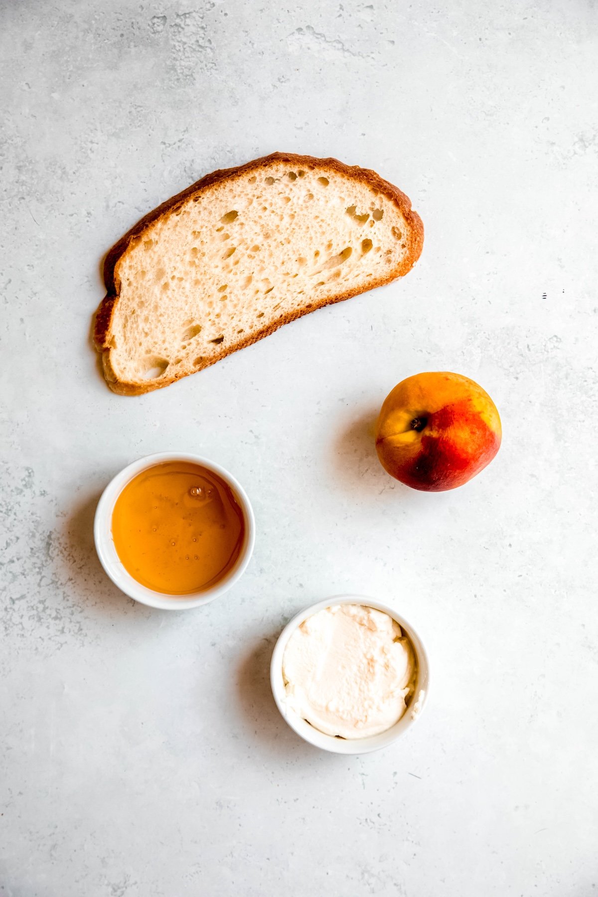 crusty bread, honey, ricotta, and a fresh peach measured out for making peach toast recipe.