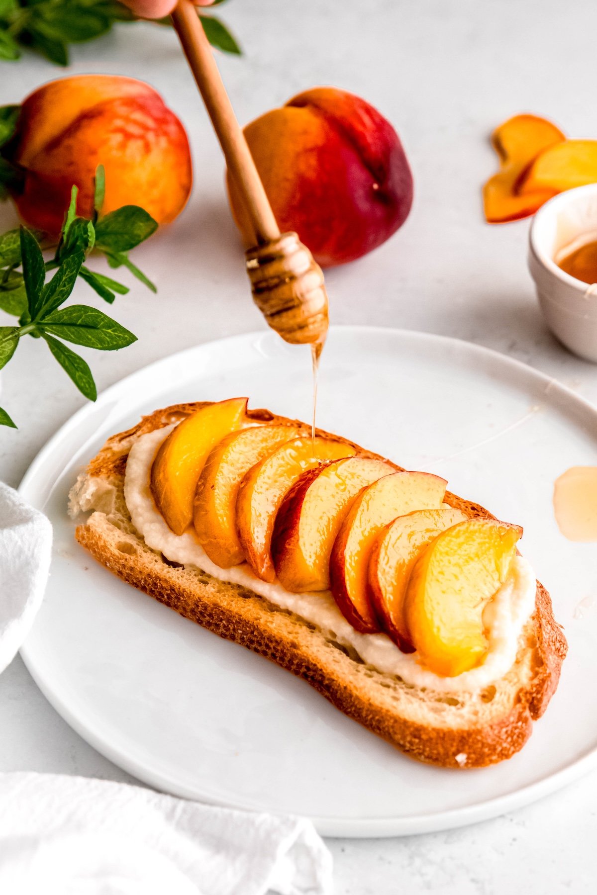 action shot of a hand using a honey dipper to drizzle honey atop the peach toast.