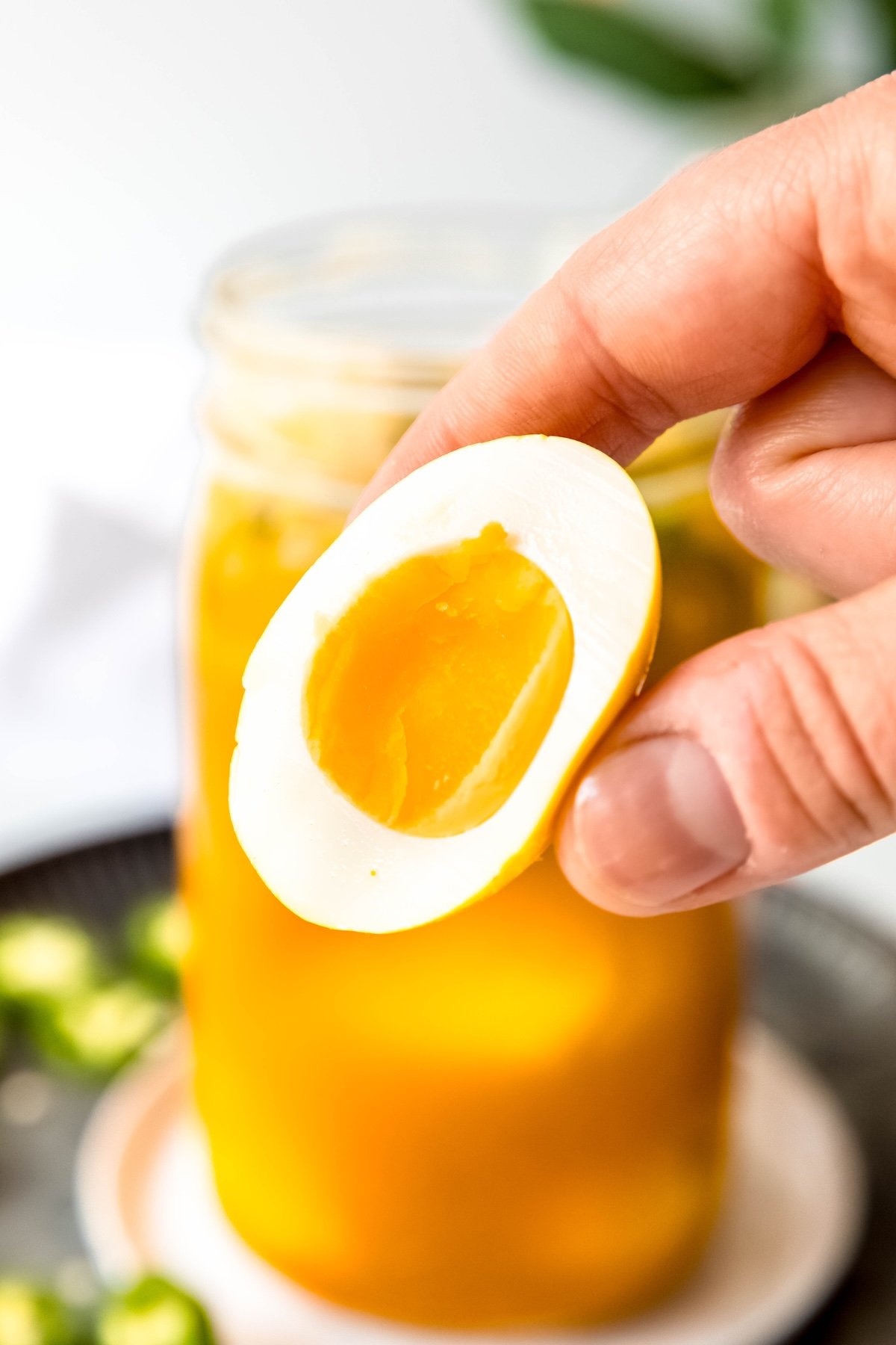 hand holding a halved soft-boiled jalapeño pickled egg to show the jammy yellow yolk; the color matches the bright saffron hue of the turmeric pickling liquid.