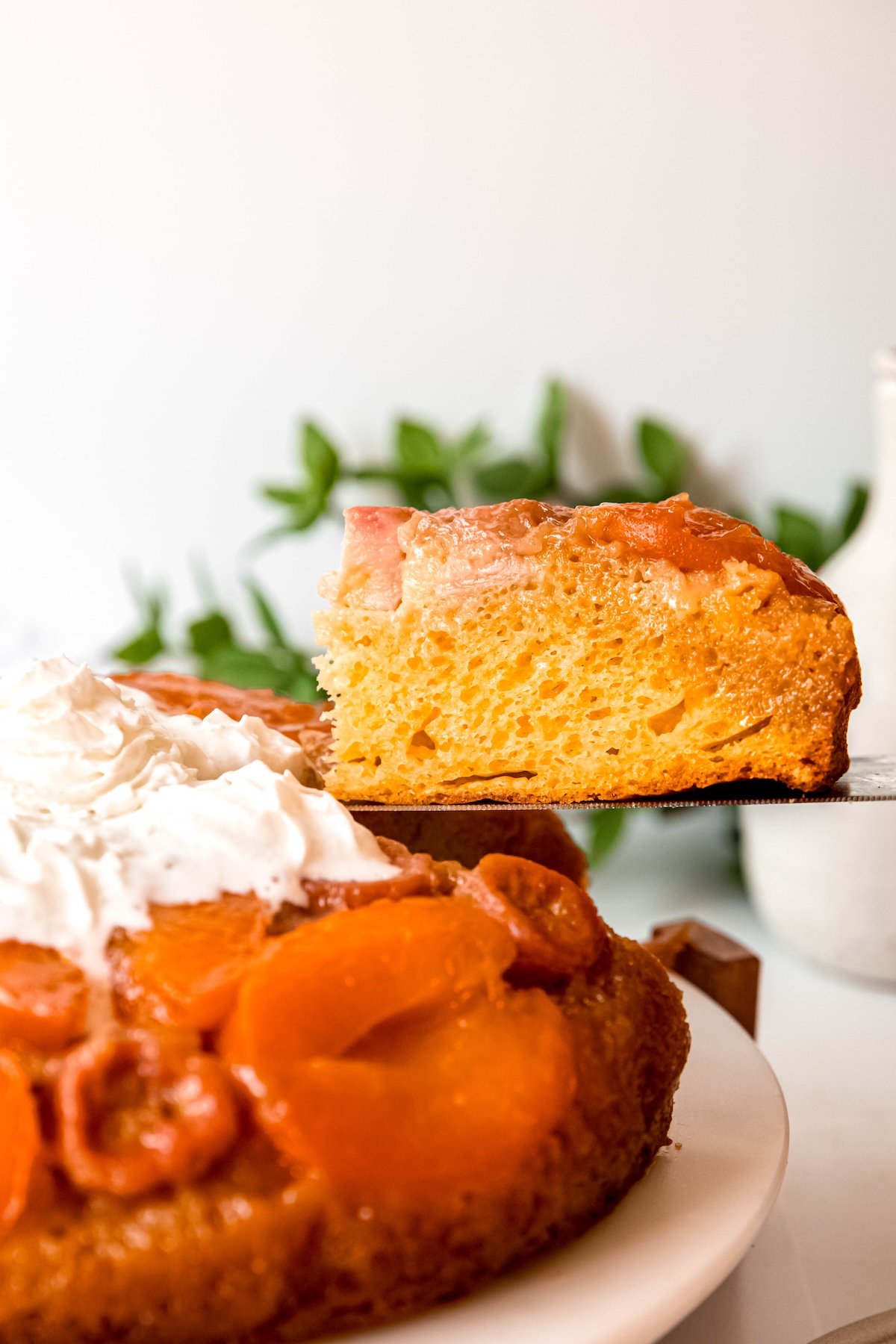 cake server lifting a slice of amaretto apricot banana upside down cake from the right side of the cake.