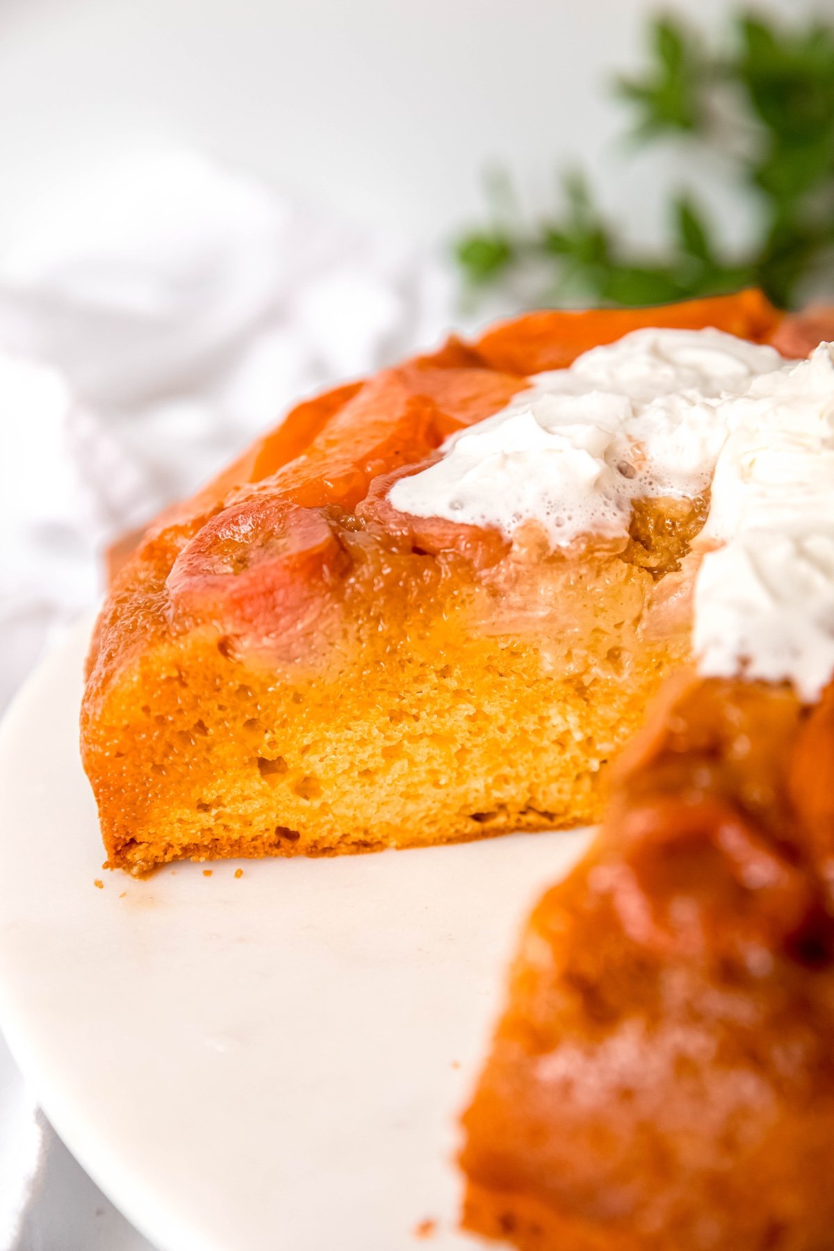 closeup shot of an almond apricot upside down cake with bananas with a few slices taken out; you can see the fluffy cake topped with a juicy fruit and caramel layer than soaks down into the top ⅓ of the cake.