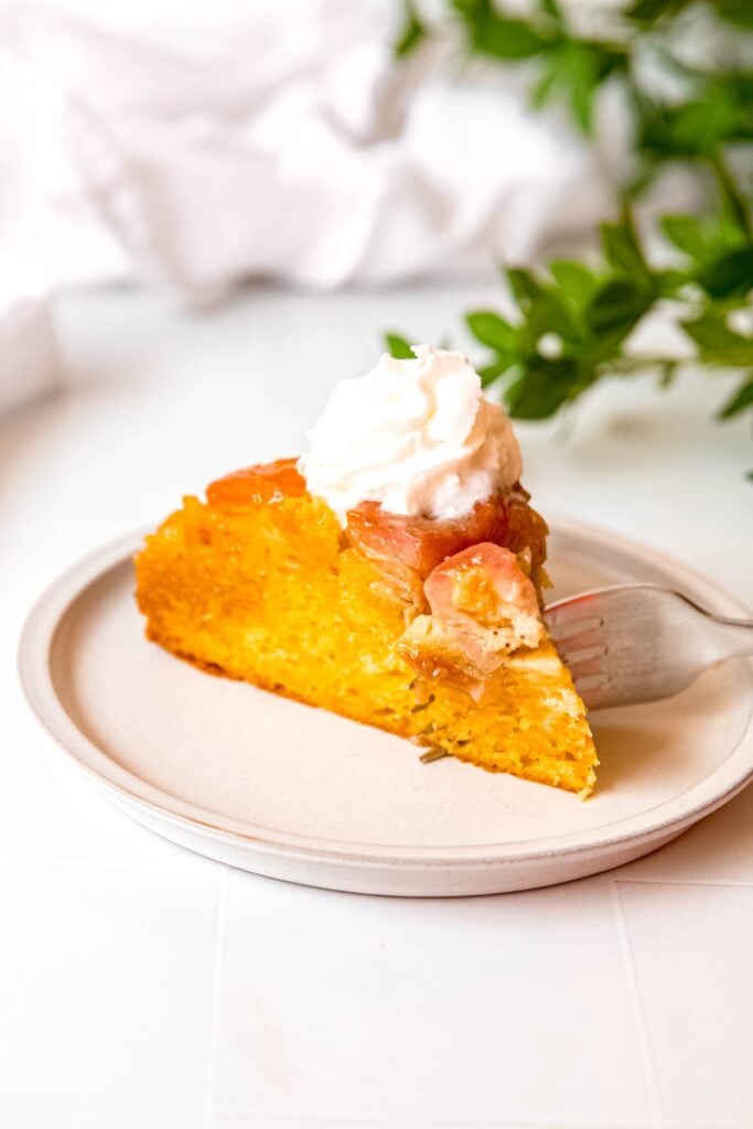 silver fork taking a bite from the tip of a slice of almond apricot banana upside down cake.