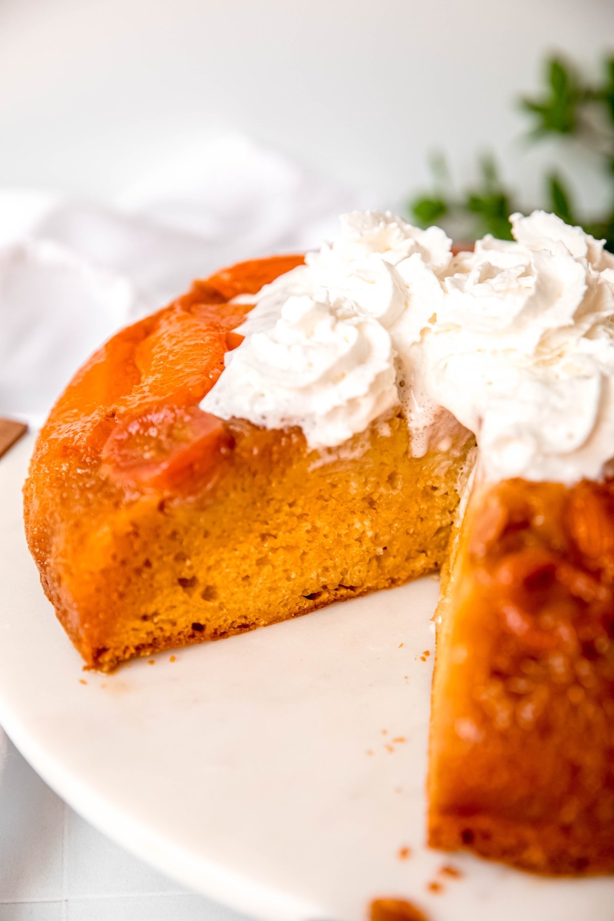 closeup shot of a banana apricot upside down cake with a slice taken out so you can see the juicy fruit and caramel layer, melting whipped cream, and fluffy yellow cake layer.