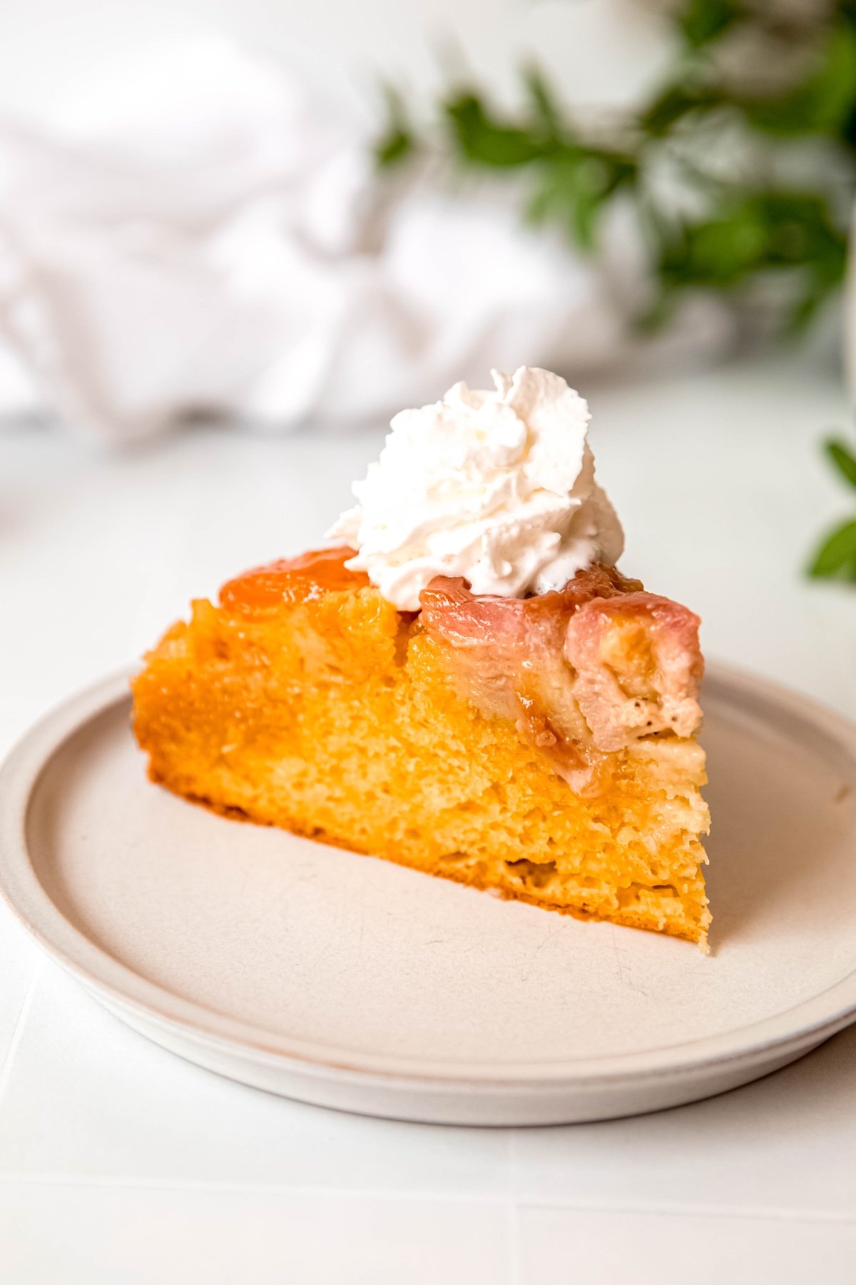 slice of cake mix upside down banana apricot almond cake on a white dessert plate with a squirt of whipped cream on top.