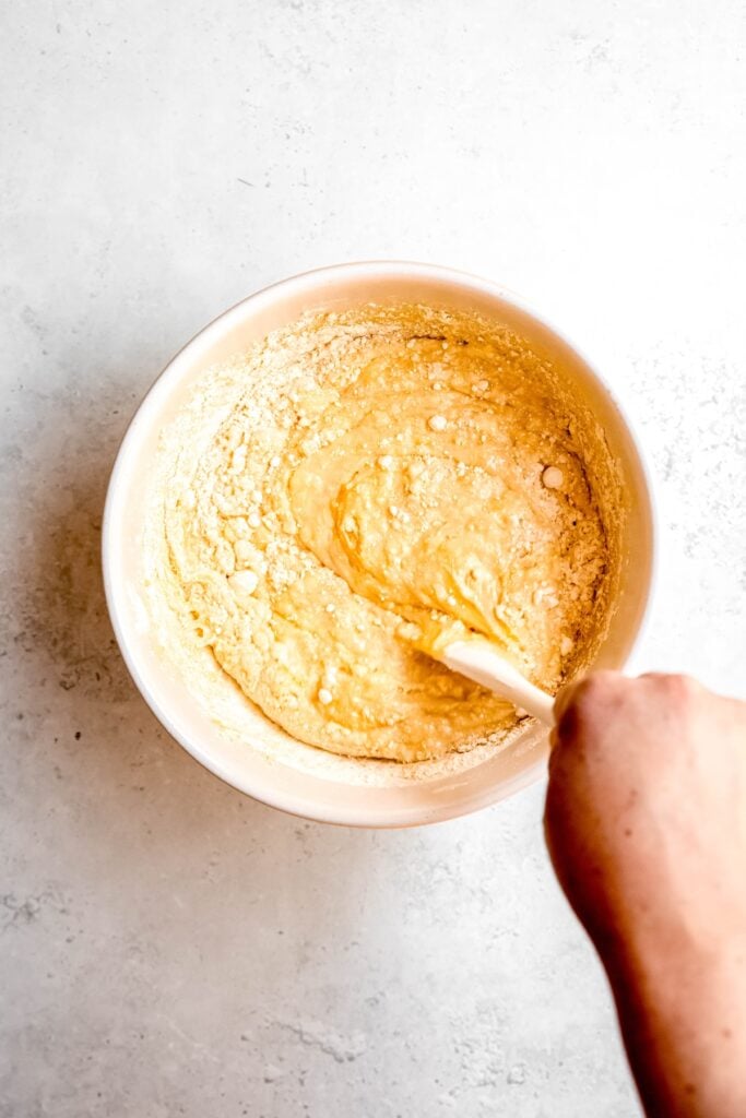 action shot of a hand using a wooden spoon to mix the doctored cake mix batter.