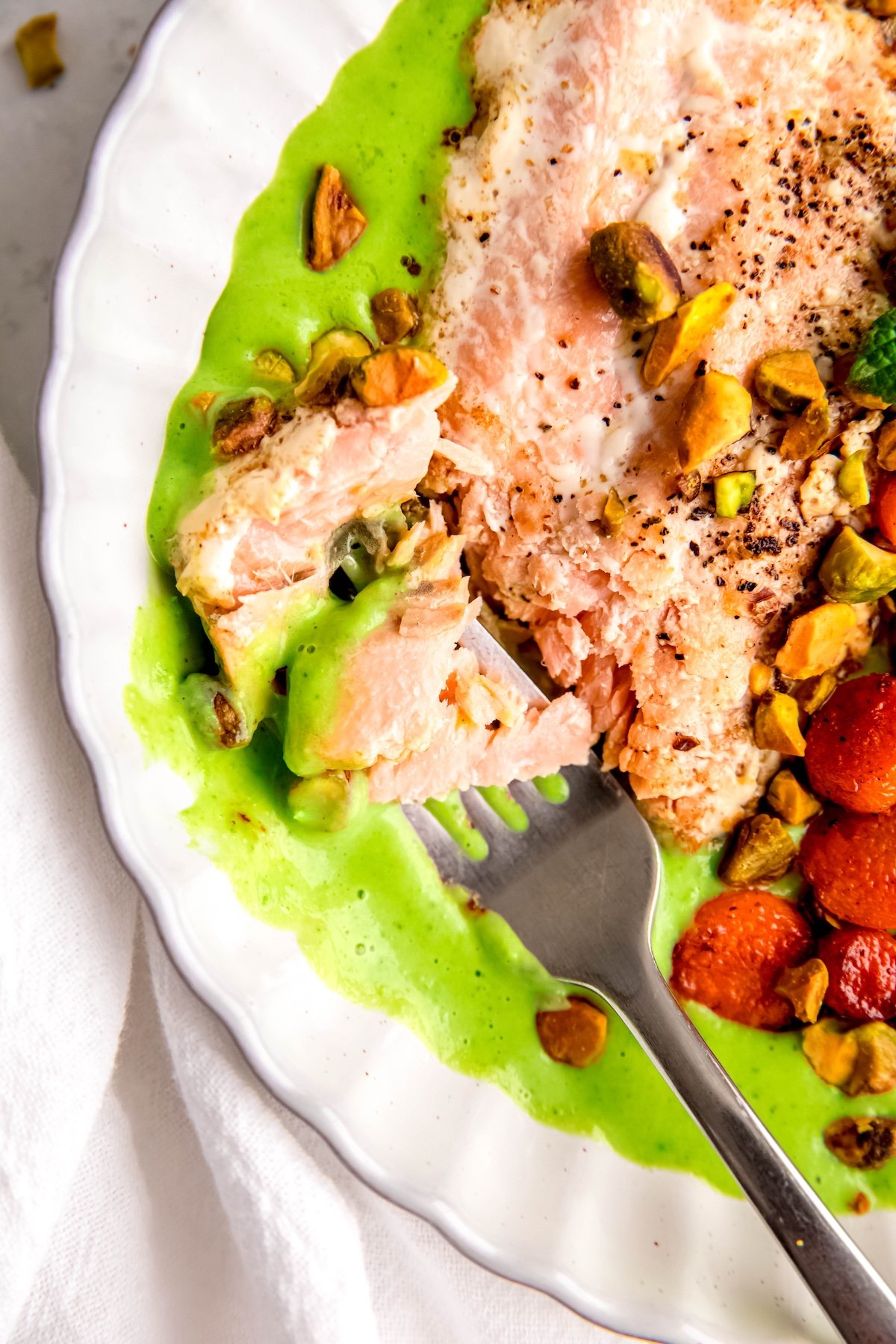 closeup overhead shot of the left half of a plate of one-pan salmon with mint pea puree and roasted carrots with a silver fork taking a bite.