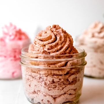 3 flavors of whipped cream dispenser recipes in clear jars on a table; chocolate is in the front, strawberry and cinnamon in the back.