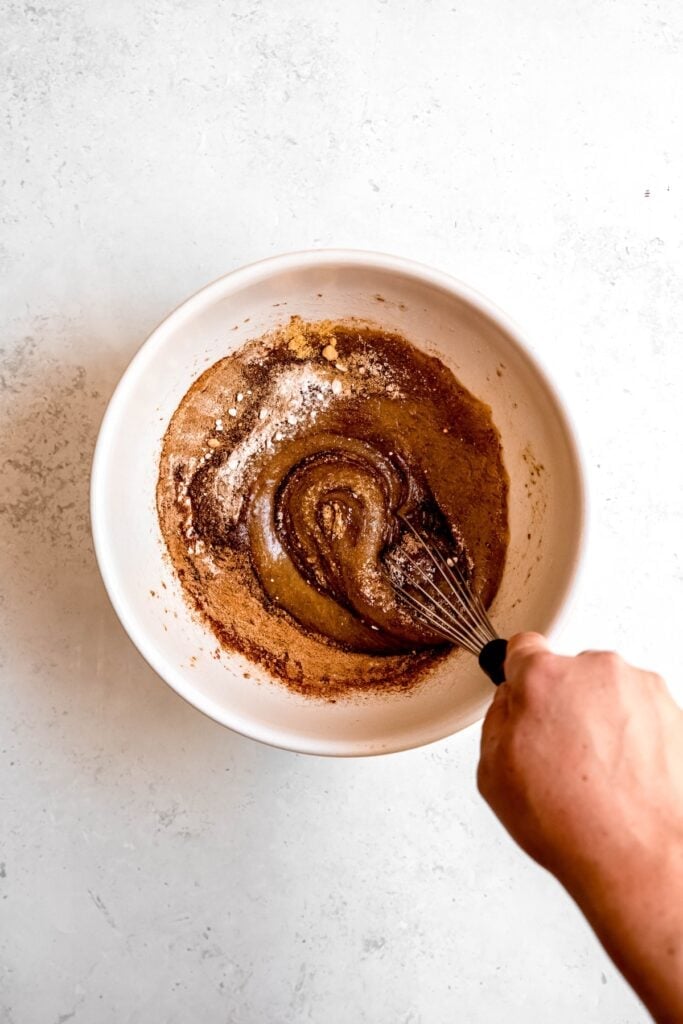 action shot of a hand whisking the leaveners and seasonings into the wet ingredients.
