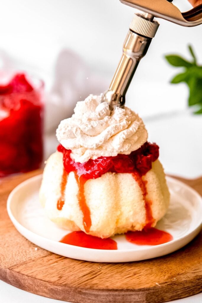 action shot of the whipped cream dispenser dispensing whipped cream onto a strawberry shortcake; the nozzle creates a pretty piped pattern in the firm peaks.