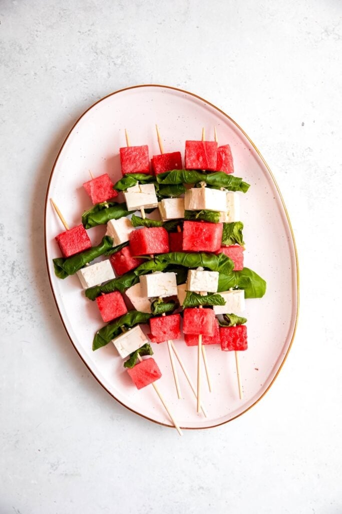assembled watermelon skewers with feta and herbs on a white serving platter before dressing with lime juice, olive oil, flaky salt, and pepper.
