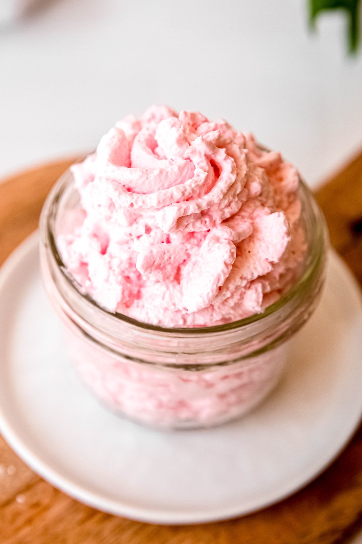 closeup shot of pretty pink strawberry flavored whipped cream made in a whipped cream dispenser piped into a glass jar on a white plate.