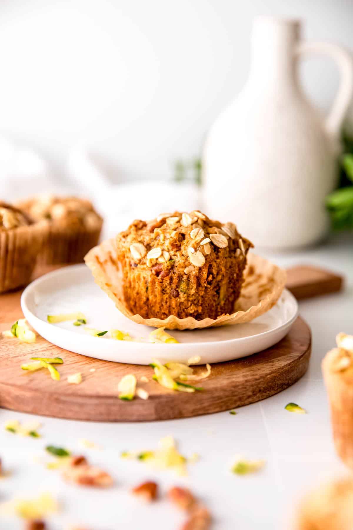 half unwrapped vegan zucchini muffin on a plate surrounded by other muffins topped with rolled oats.
