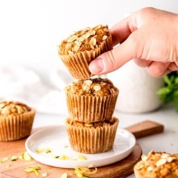 hand taking the top of a stack of three vegan zucchini muffins with oats, whole wheat, and flaxseed.