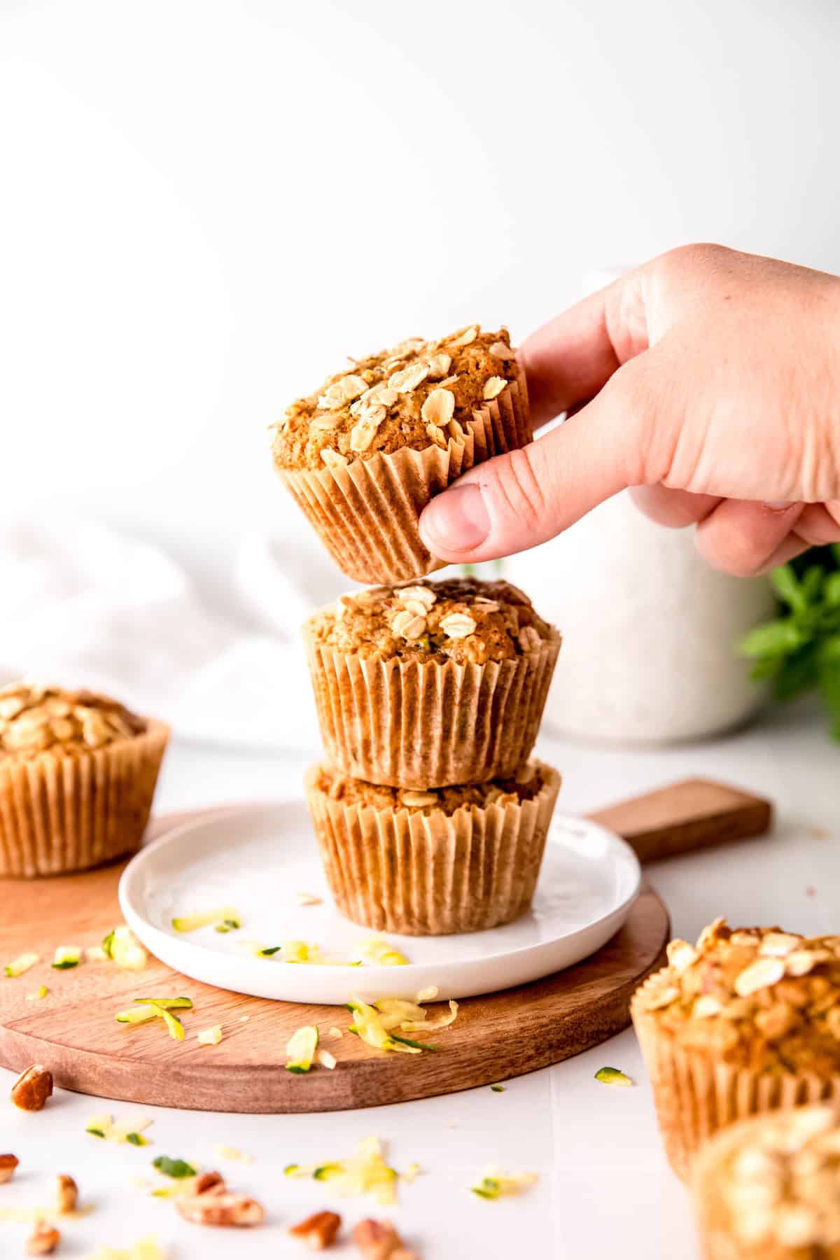 hand taking the top of a stack of three vegan zucchini muffins with oats, whole wheat, and flaxseed.
