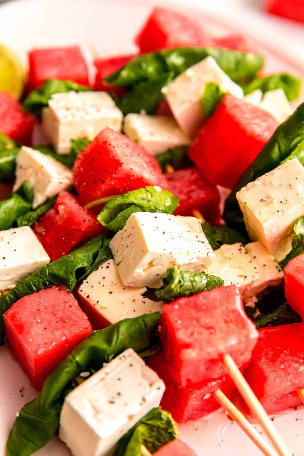closeup shot of a pile of watermelon feta appetizer skewers on a plate showing the pretty pink, white, and green color combo.