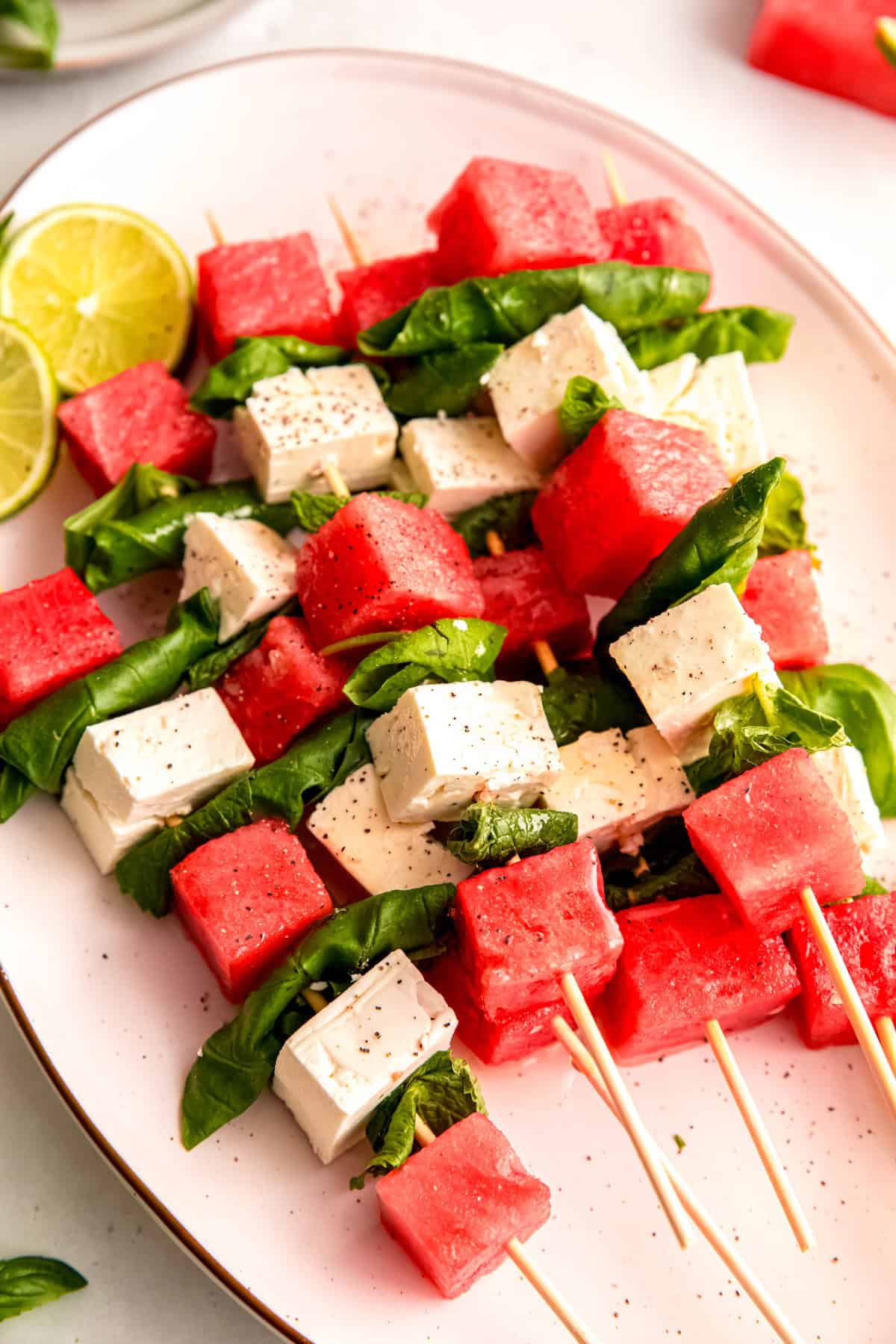45 degree angle shot of watermelon feta salad-on-a-stick skewers on a white serving platter.