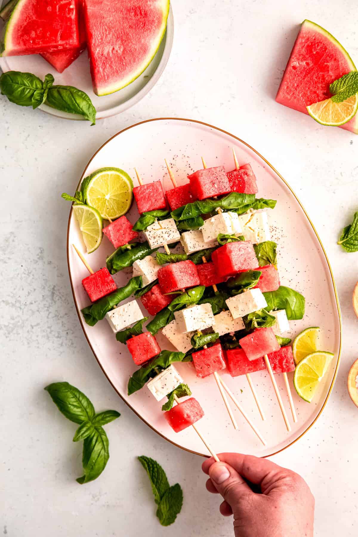 hand grabbing a watermelon skewer from the platter.