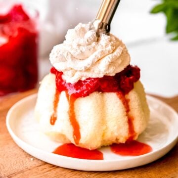 square closeup hero image of a strawberry shortcake being topped with dispenser whipped cream.