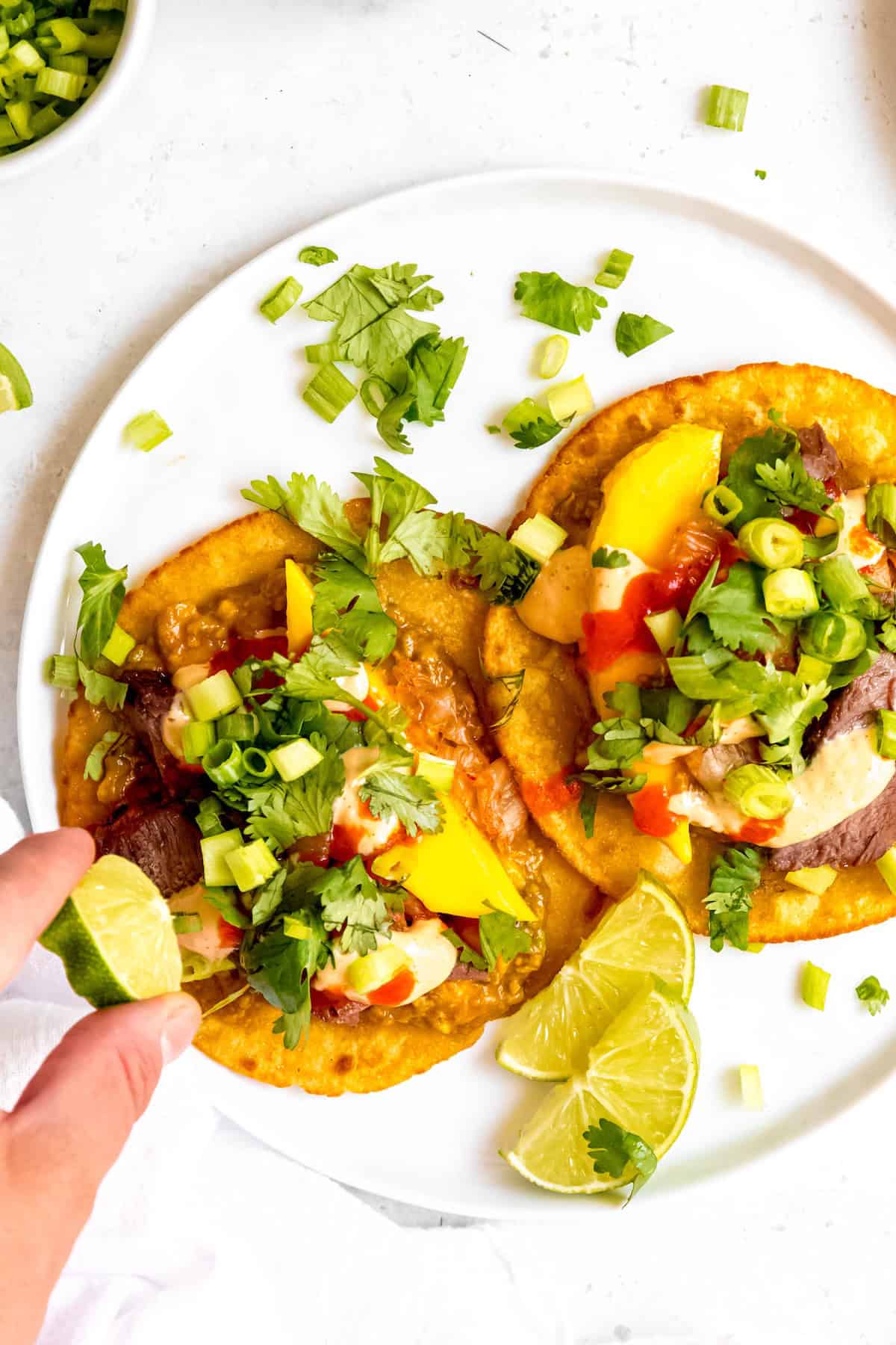action shot of a hand squeezing a lime wedge over Korean-inspired gochujang skirt steak tacos.