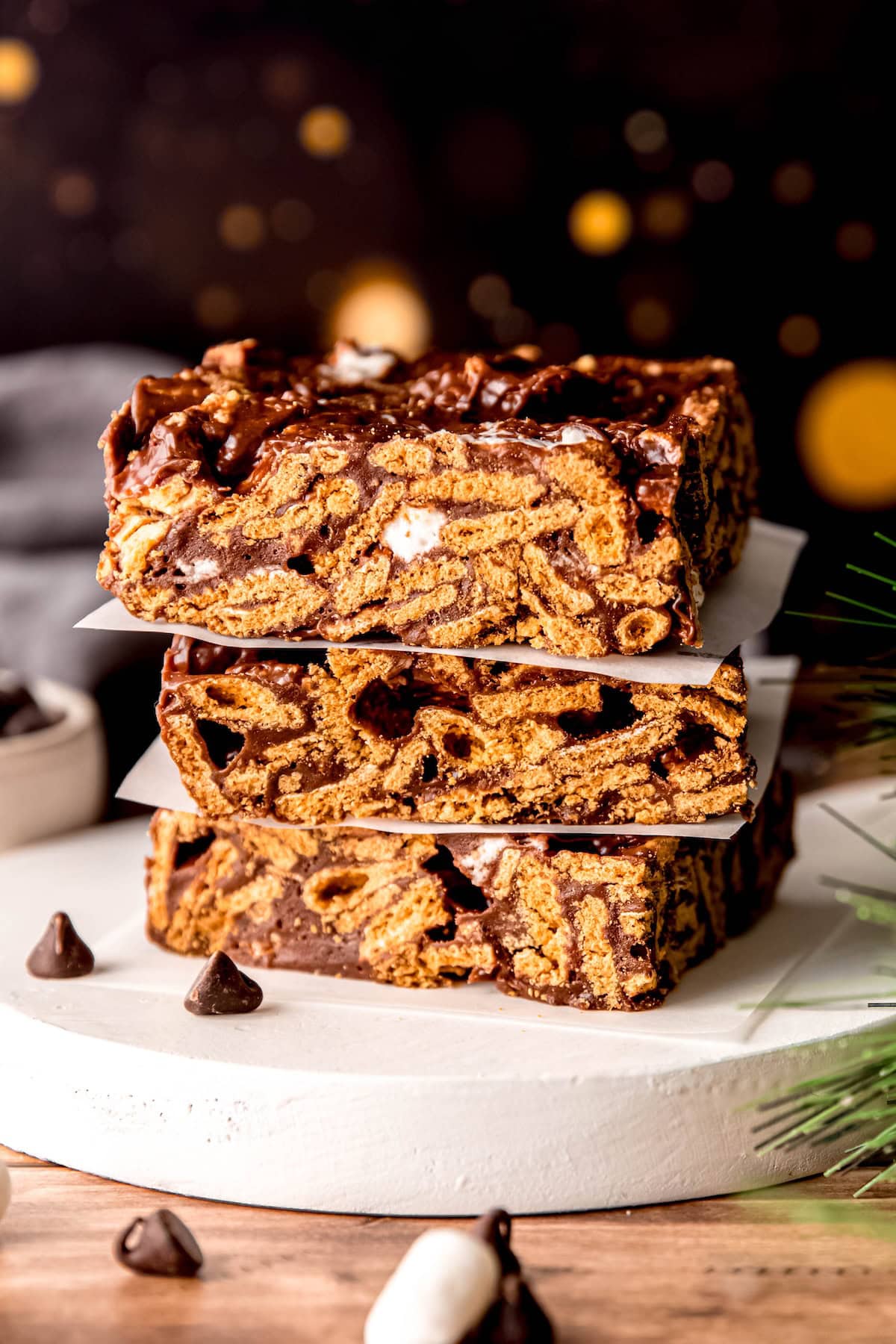 closeup side on shot of a stack of golden graham smores bars on a wooden table in front of a dark backdrop with golden orbs that looks like they come from a campfire.