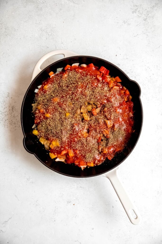 herbs and tomato sauce added to the skillet with the sautéed aromatics.