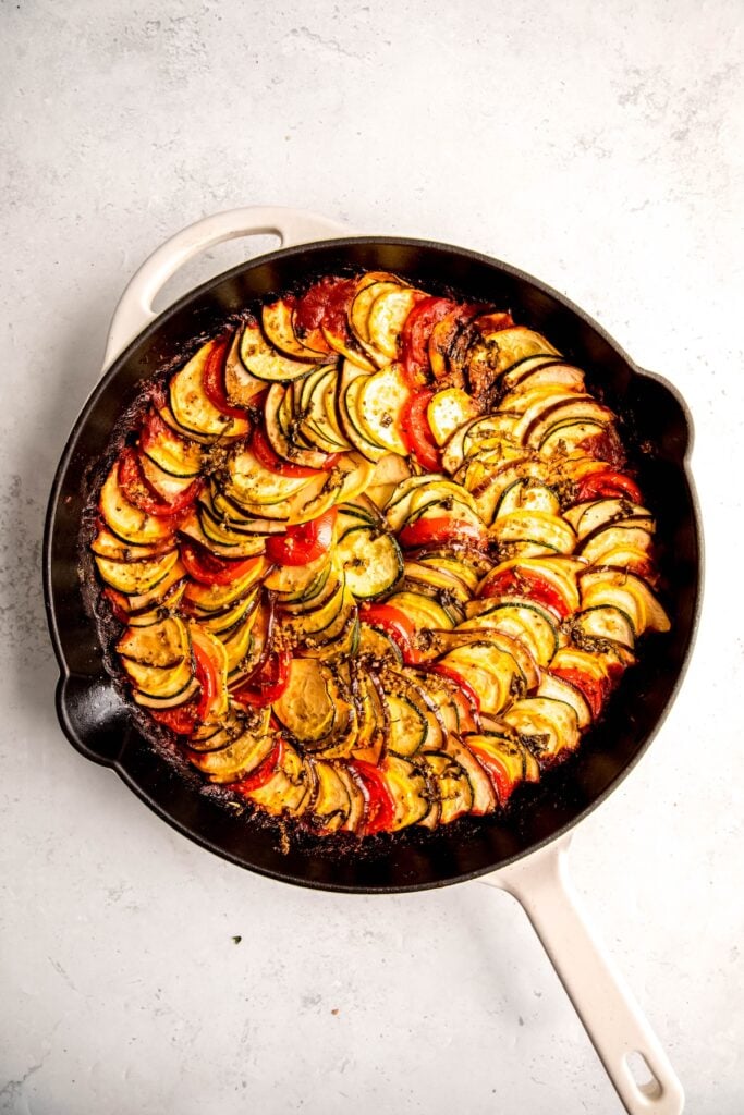 baked disney-style ratatouille in a cast iron skillet on a white table.