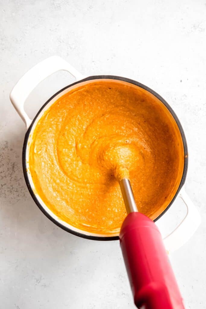 action shot of an immersion blender blending the chicken, rice and pumpkin mixture together.