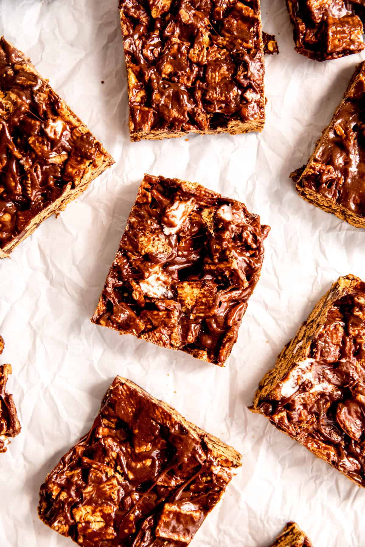overhead shot of indoor smores bars on a white surface; you can see melty, stretchy pieces of marshmallows, graham cereal, and a shiny chocolatey glaze holding it all together.