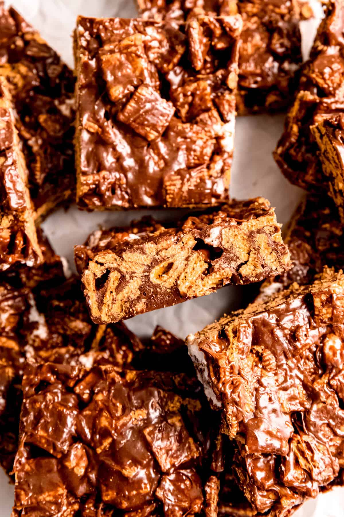 closeup overhead shot of indoor smores bars made with golden grahams cereal; the tops are all shiny from the chocolate marshmallow mix, but one bar is turned on the side to show the texture of the graham cereal and sticky marshmallows stirred throughout.