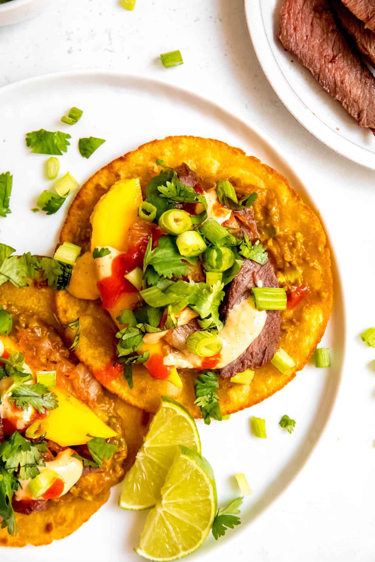 closeup overhead shot of the right half of a plate of two korean bbq beef tacos made with grilled skirt steak.