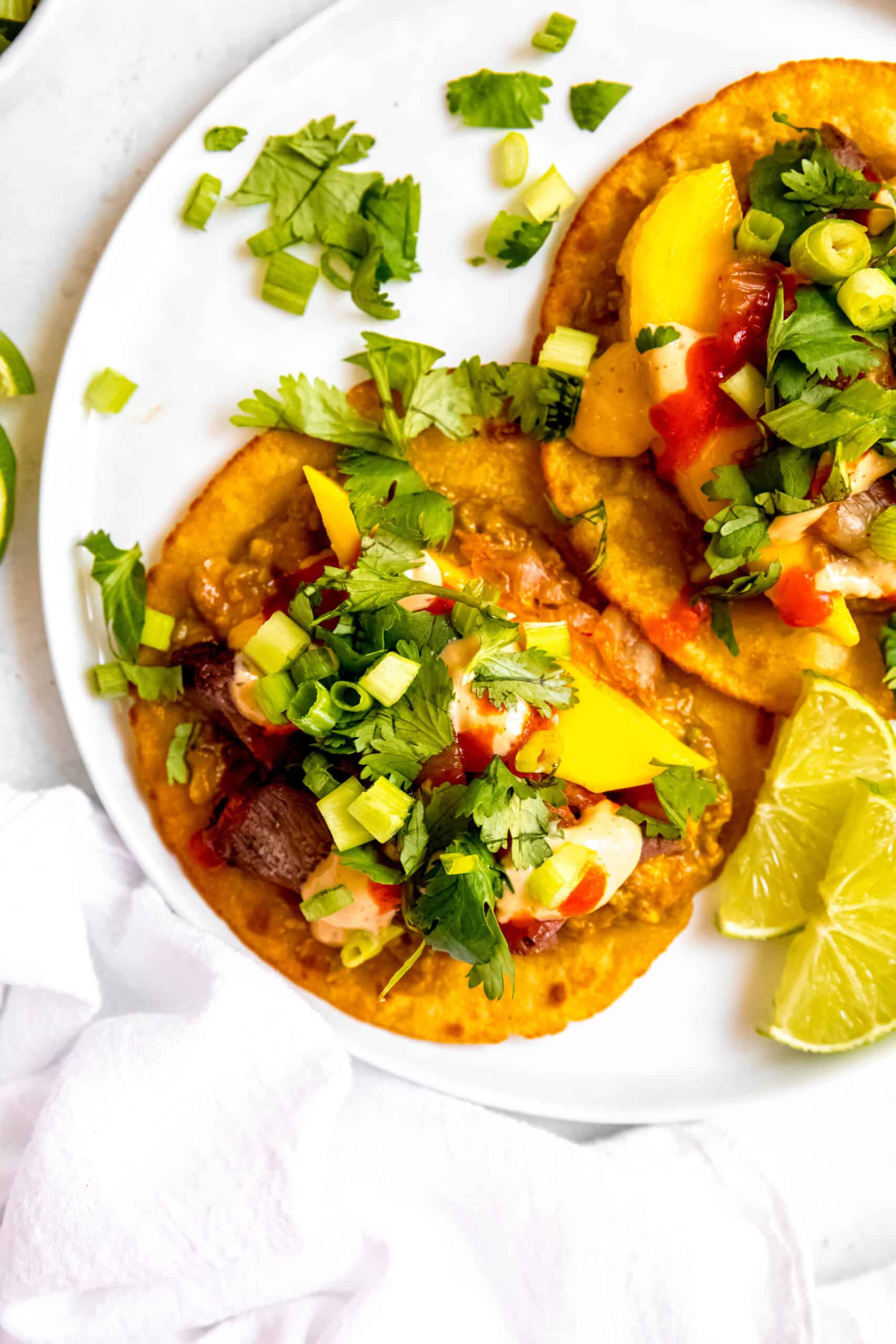 two korean inspired skirt steak tacos with mango, gochujang, and avocado on a white plate.