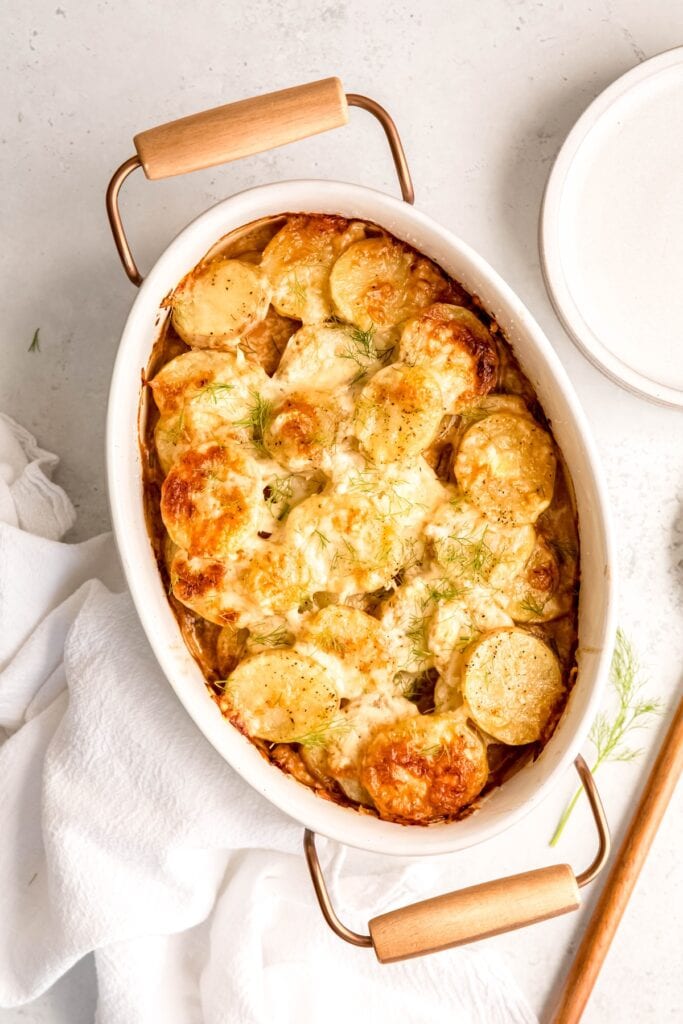 white marble table with a casserole dish filled with fennel potato au gratin.
